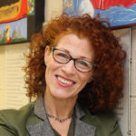 Laura McCullough headshot, she has red curly hair, wearing glasses, has a big smile, and is wearing a green and gray jacket.