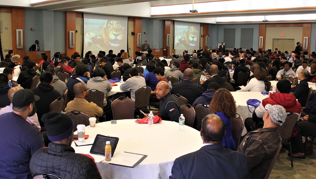Event speach photographed from the audience perspective, seated and in the middle of a large group of people.