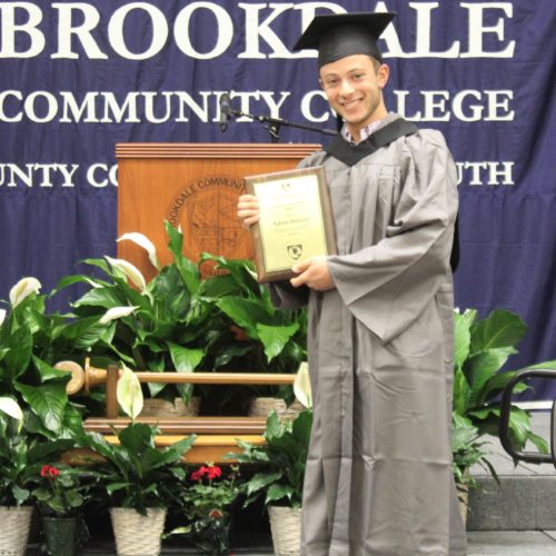 Adam Meliani holding award in cap and gown at graduation
