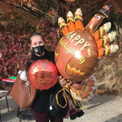 girl with a mask on holding balloons, one is a turkey balloon.