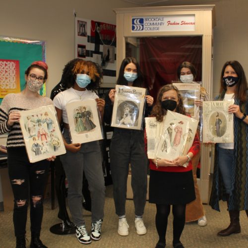 group of four students and two faculty members holding up a collection of fashion publications in the classroom