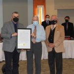 three men in suit and tie with masks on holding a proclamation to honor the middle man.