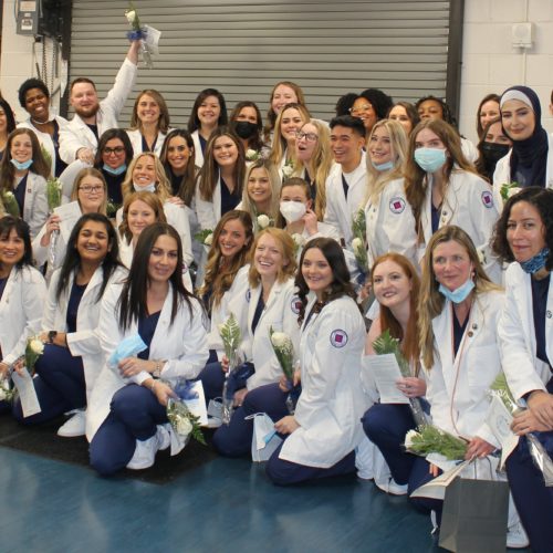 group of nursing students in their white jackets cheering and smiling after graduation