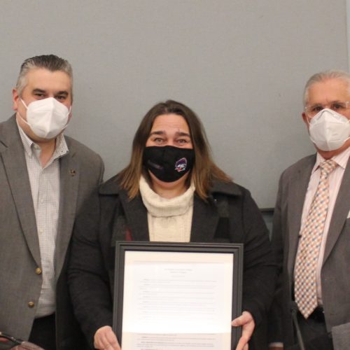 two men in a suit jacket, and a woman between them. The woman is holding a proclamation