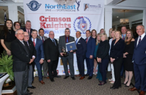 A group of people wearing suits and ties with man holding award in the center of the group. All are wearing a smile.