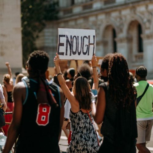 women walking in protest, one woman holding a sign that says "Enough"