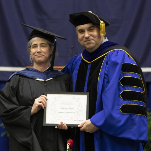 A woman and man in their academic gowns and hats presenting the honorary degree