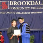 woman in black Regalia receiving an award from President of College in his blue Regalia