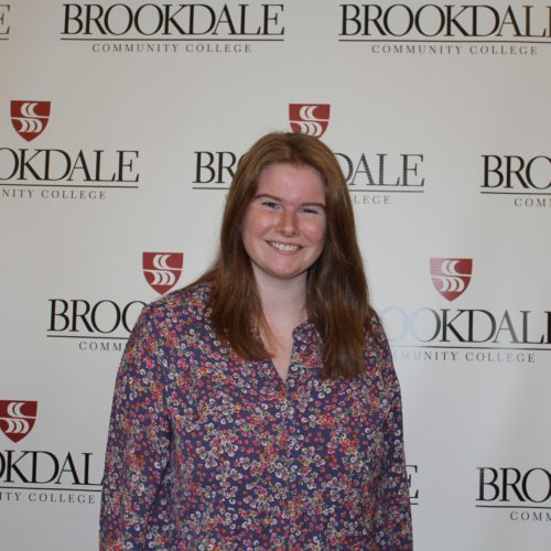 Woman with long red hair wearing a smile and a printed dress with a Brookdale backdrop behind her.