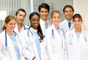 Seven men and women wearing white nursing jackets and stethoscopes around their necks