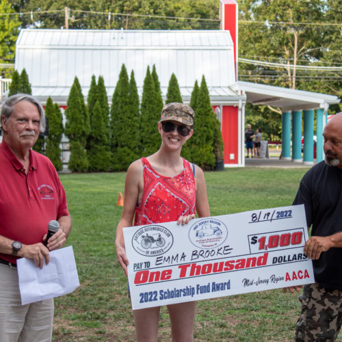 A man and a woman holding a big check and another man in a red shirt standing by.