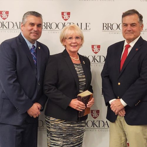 Two men in suit and tie with a woman smiling in the middle. Brookdale return logos in background.