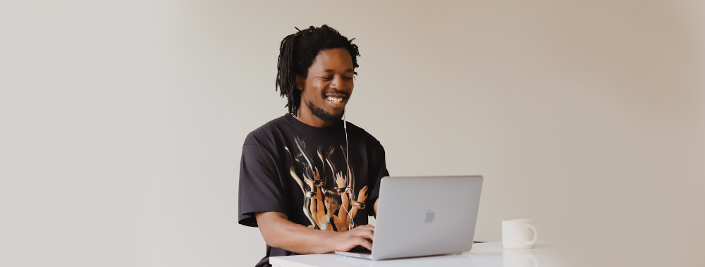 man with dark skin with his computer open and a smile on his face.