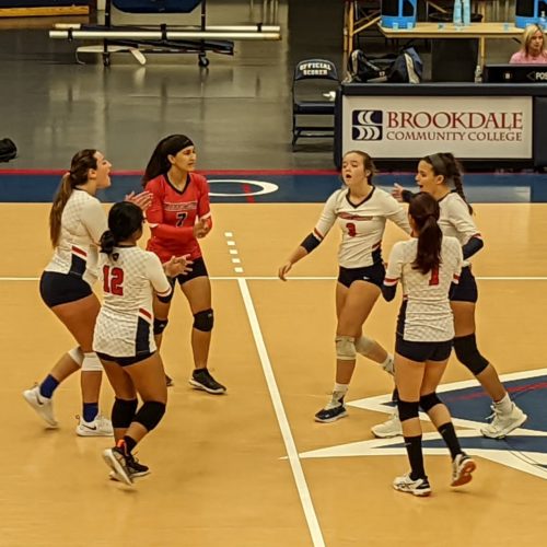 group of women playing volleyball coming together for a group cheer