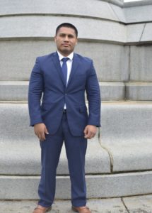 Man with a blue suit and blue tie standing in front of a cement court house building