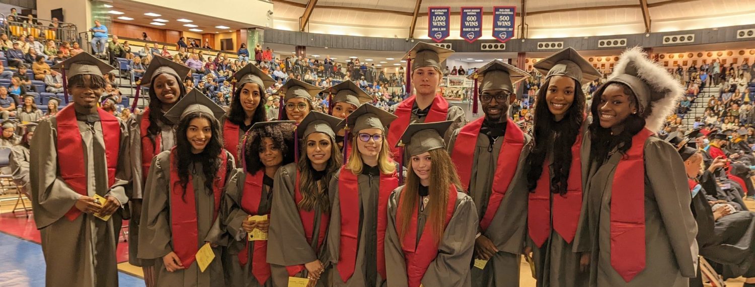 Group of High School student at graduation wearing grey robes and red stole.