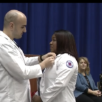 Male nurse pinning a female nurse. Both wearing their white jackets.