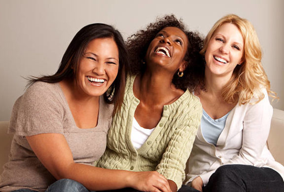 Three women sitting close together with arms around each other, laughing and smiling.
