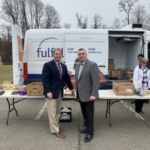 Fulfill Van at Brookdale Community College Lincroft campus. Two men standing in front of table with food and van behind them with door open to more food supplies.