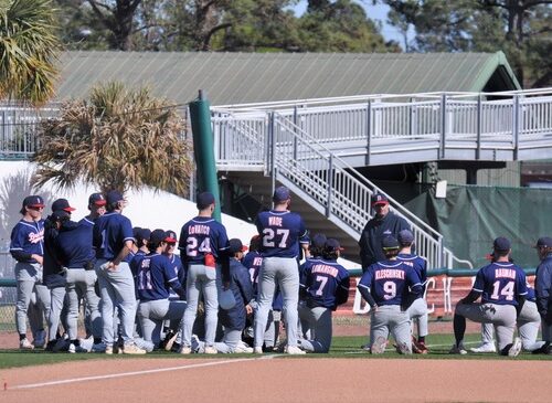 Baseball team in a huddle meeting with the coach talking to them.