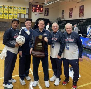 Men's basketball coaches holding the championship trophy.