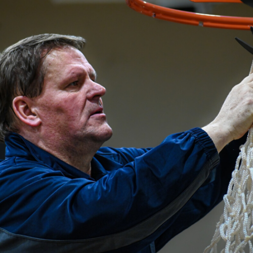 Man with dark blue jersey on cutting the ropes on a basketball net.