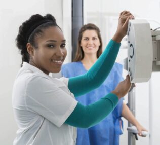 Woman at the x-ray machine with another woman looking on.