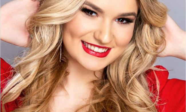 Woman with long blond hair wearing a red dress and red lipstick. Her hands are behind her head.