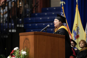 Donna Tango speaking at the podium at Commencement ceremony wearing cap and gown.