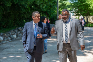 Two men wearing a suit and tie, talking and walking down the path with people following behind.