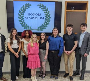 Eight students in front of Honors Symposium sign.