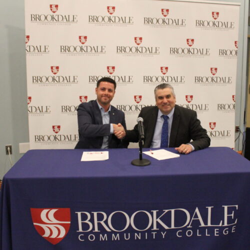 Two men wearing a suit jacket at a table shaking hands.