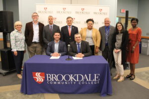 Board of Trustees gathered around the table where President Dr. David M. Stout and Regional Recruiter Sam Cammarata are signing MOU.