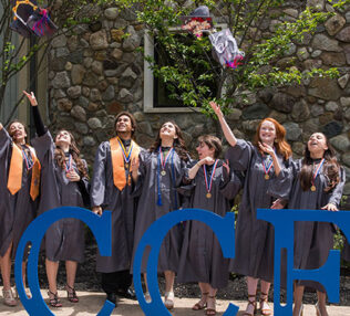 10 students in graduation gowns throwing their hats behind the Success sculpture.