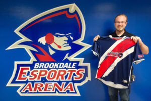 Esports director holding the Varsity Jersey in front of logo just outside the Arena.