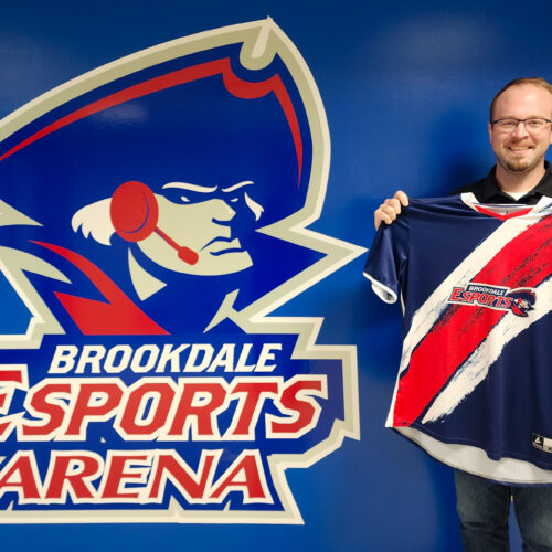 Esports director holding the Varsity Jersey in front of logo just outside the Arena.