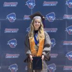 Woman with blond hair wearing her graduation cap, gown and regalia.