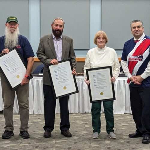 Five adults holding Proclamations at a Board meeting recognition,