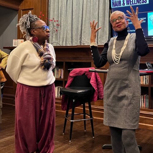 Two black women on a stage talking and one is gesturing with her hands.