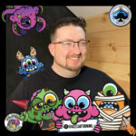 Man with facial hair and glasses wearing a black t shirt with monsters all around the frame.