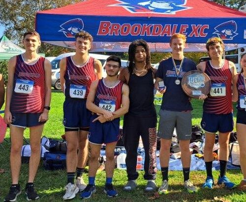 Nine cross country runners pose for photo in front of Brookdale tent.