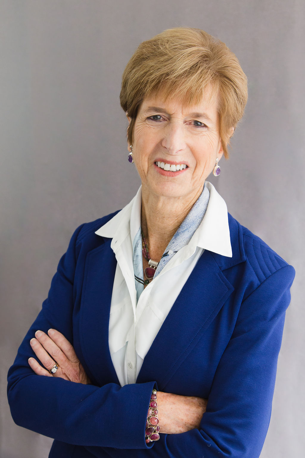 hristine Todd Whitman Woman with short blond hair wearing a royal blue suit jacket, white shirt and scarf. Her arms are crossed and she is smiling.