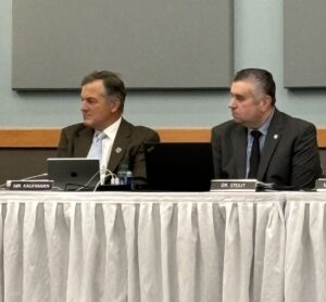 Two men in suit and ties sitting at the dais of Board of Trustees meeting.