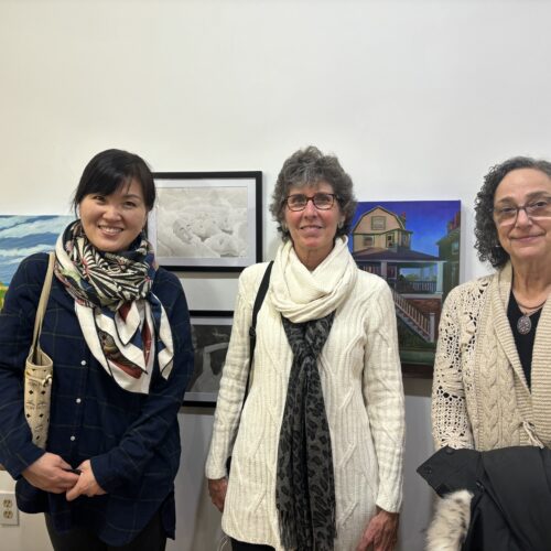 Three woman standing in front of art work on the walls.