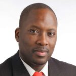 Male wearing a dark suit and orange tie.