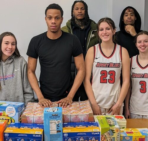 Six men and women wearing athletic wear are standing behind a table with packaged food on it.