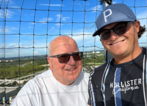 Dr. Lester Richens wearing sunglasses and white t-shirt and his grandson who is wearing baseball gear.