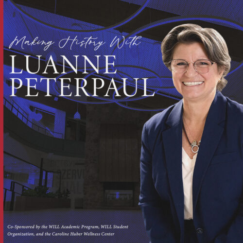 Luanne Peterpaul wearing a navy blazer and white shirt. She has short brown hair, glasses and a smile on her face.
