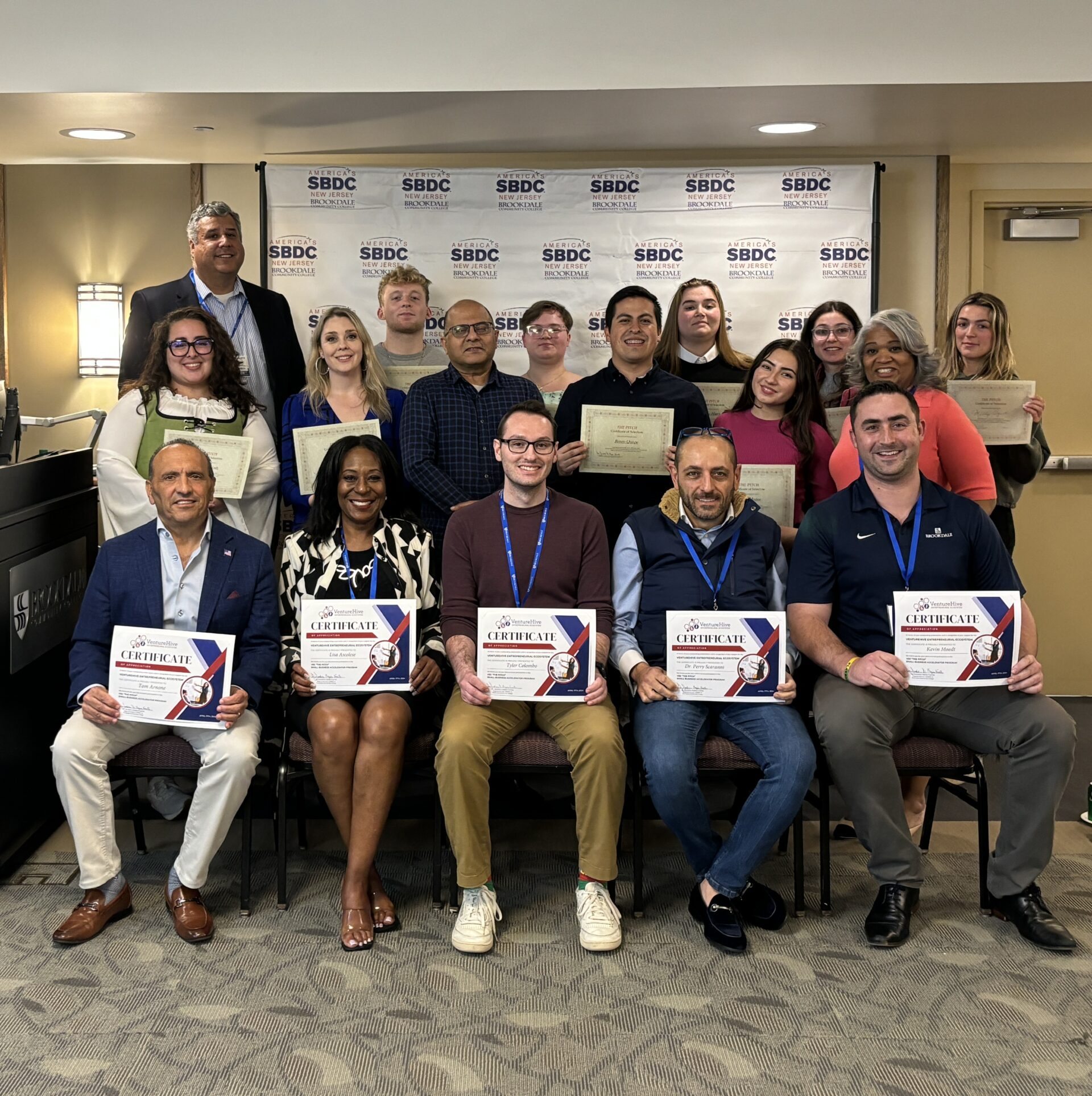 Group of men and women standing and sitting holding their certificates of participation.