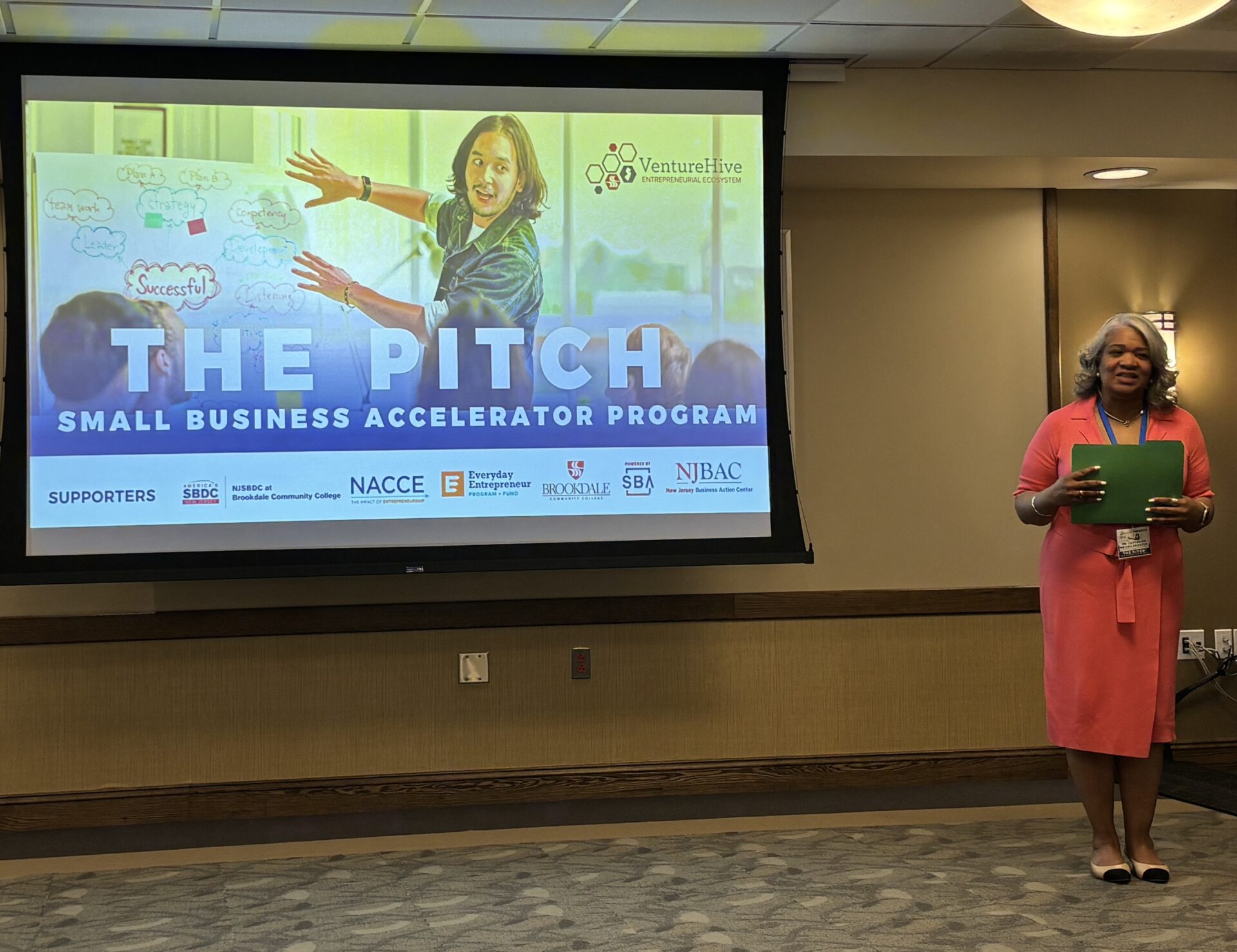 Woman wearing an orange dress with screen behind her that says The Pitch.